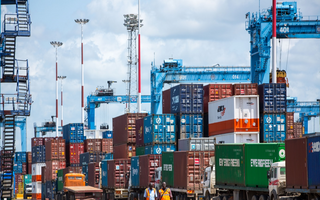 Two people walking beside a row of containers in harbor