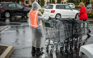 Essential worker at grocery store in rain coat collecting shopping carts in the rain