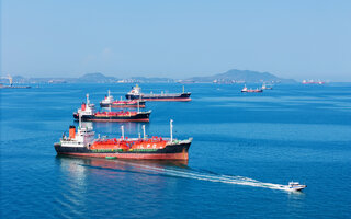 LPG gas and oil tanker ships anchored in the ocean, with a fast patrol boat in the foreground