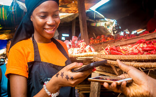 young african woman selling tomatoes in a local african market receiving payment via mobile phone transfer
