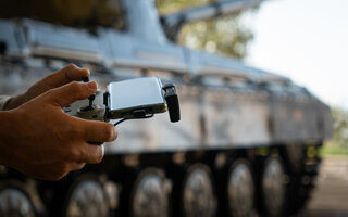 man with a UAV control panel in his hands, a drone flying above the tank in the background in nature