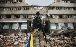 Ukrainian military woman with the Ukrainian flag in her hands on the background of an exploded house