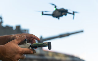 man with a UAV control panel in his hands, a drone flying above the tank in the background in nature