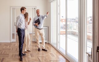 Estate agent showing a young couple the city views from an unfurnished house with a large balcony