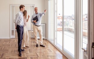 Estate agent showing a young couple the city views from an unfurnished house with a large balcony