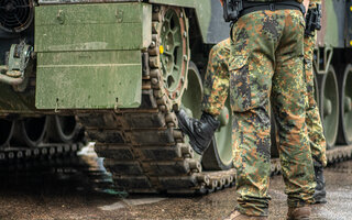 Two soldiers in camouflage uniform standing during a break under the rain near the tracks of an armoured tank, only the trousers and the boots are visible