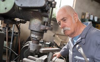 elderly worker watches processing of detail on milling machine