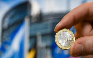 Person holding 1 Euro coin in front of EU Parliament