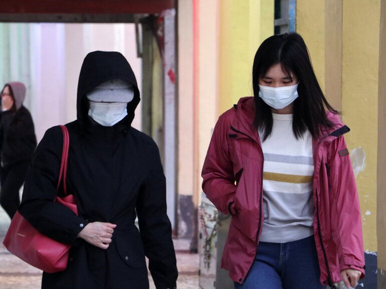 Two women walking in public wearing masks